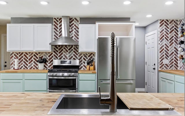 kitchen with tasteful backsplash, butcher block countertops, wall chimney exhaust hood, appliances with stainless steel finishes, and green cabinets