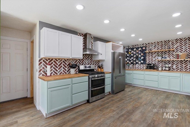 kitchen featuring appliances with stainless steel finishes, light hardwood / wood-style floors, wall chimney range hood, and wooden counters