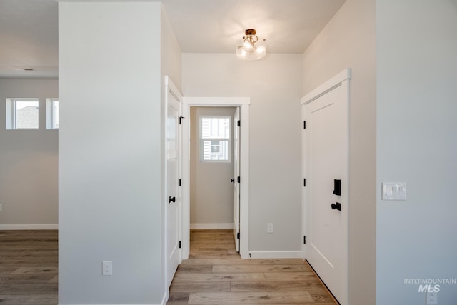 hallway with light hardwood / wood-style flooring, a healthy amount of sunlight, and a notable chandelier