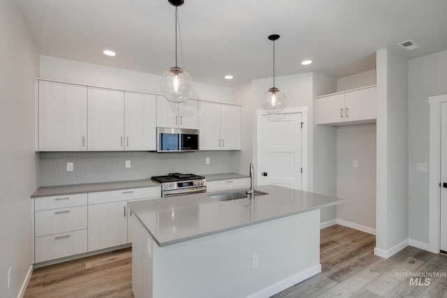 kitchen with white cabinetry, sink, hanging light fixtures, a kitchen island with sink, and appliances with stainless steel finishes