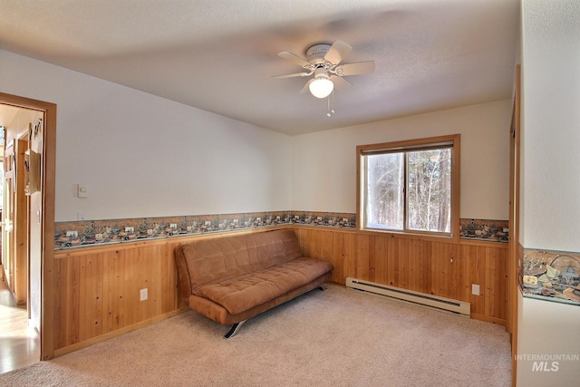 sitting room with ceiling fan, wood walls, light carpet, and a baseboard heating unit