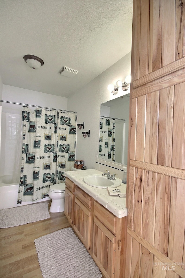 full bathroom with shower / tub combo with curtain, hardwood / wood-style floors, vanity, a textured ceiling, and toilet