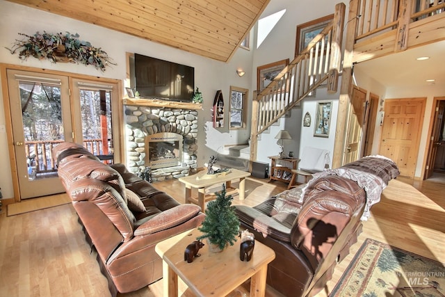 living room featuring high vaulted ceiling, a stone fireplace, light hardwood / wood-style floors, and wooden ceiling