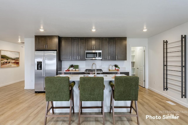 kitchen featuring a breakfast bar area, appliances with stainless steel finishes, dark brown cabinets, and light wood-type flooring