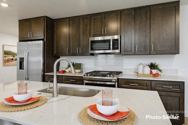 kitchen with light stone countertops, stainless steel appliances, a sink, and dark brown cabinetry