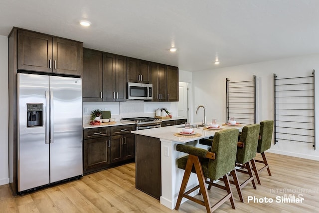 kitchen with a kitchen bar, appliances with stainless steel finishes, light wood finished floors, and a sink