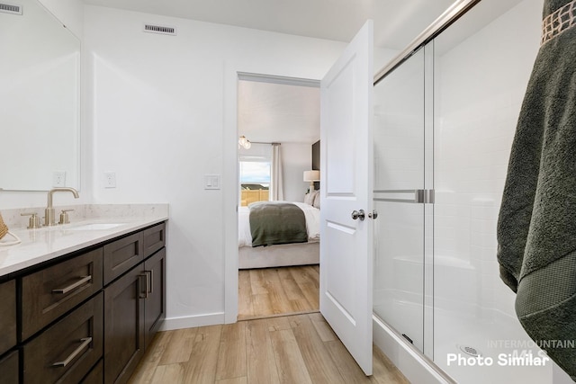 ensuite bathroom with visible vents, connected bathroom, vanity, wood finished floors, and a stall shower