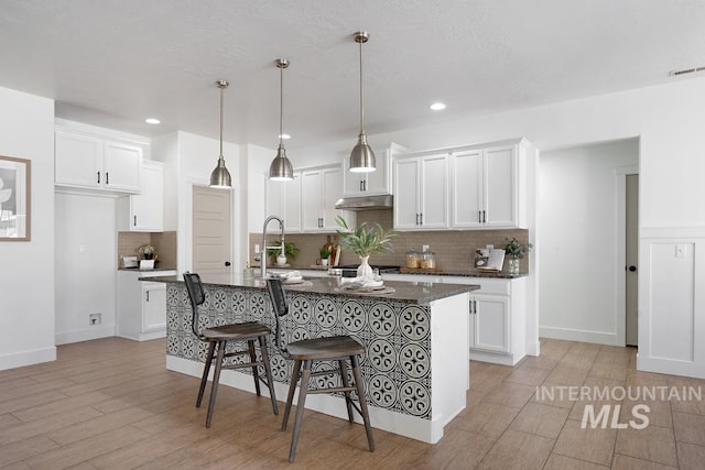 kitchen with under cabinet range hood, tasteful backsplash, white cabinetry, a kitchen breakfast bar, and recessed lighting