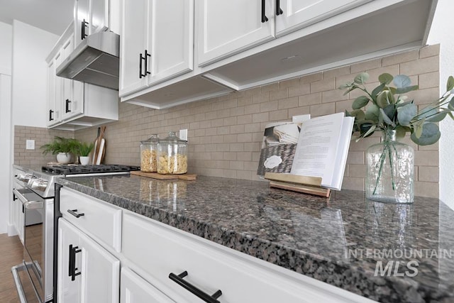 kitchen with stainless steel range with gas cooktop, under cabinet range hood, decorative backsplash, white cabinetry, and dark stone counters