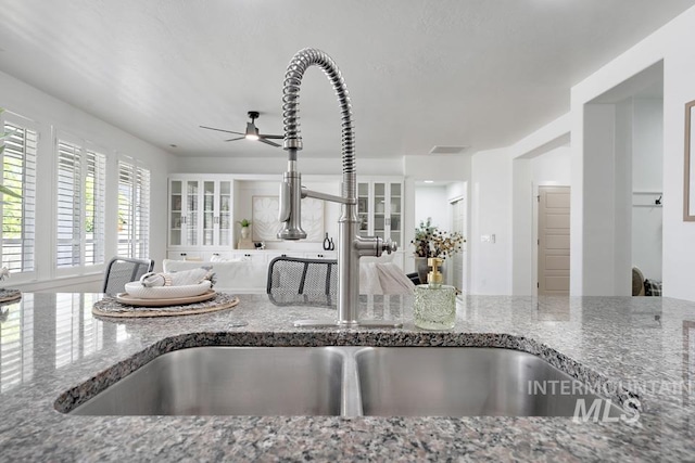 kitchen view of stone countertops, a ceiling fan, and a sink