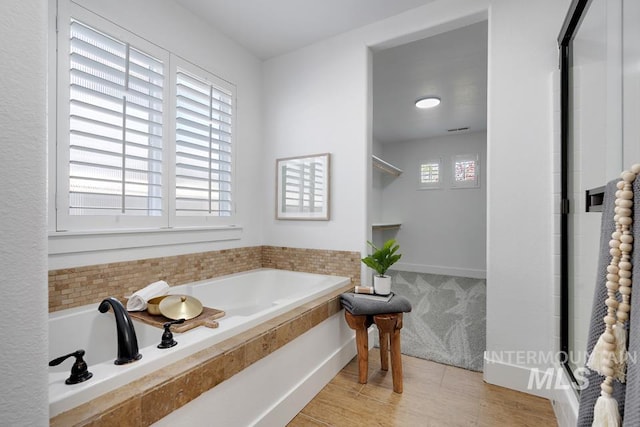 bathroom featuring a garden tub, a shower stall, and wood finished floors