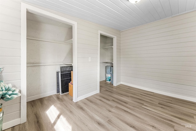 unfurnished bedroom with a closet, wooden walls, and light wood-type flooring