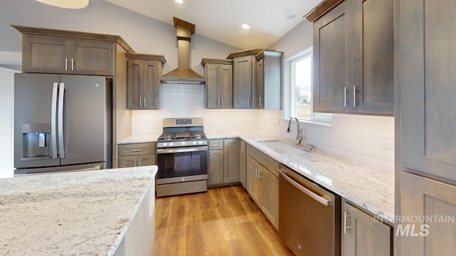 kitchen featuring vaulted ceiling, appliances with stainless steel finishes, tasteful backsplash, light stone counters, and wall chimney range hood