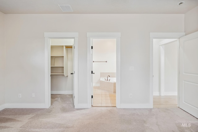 unfurnished bedroom featuring light carpet, a closet, visible vents, and a spacious closet