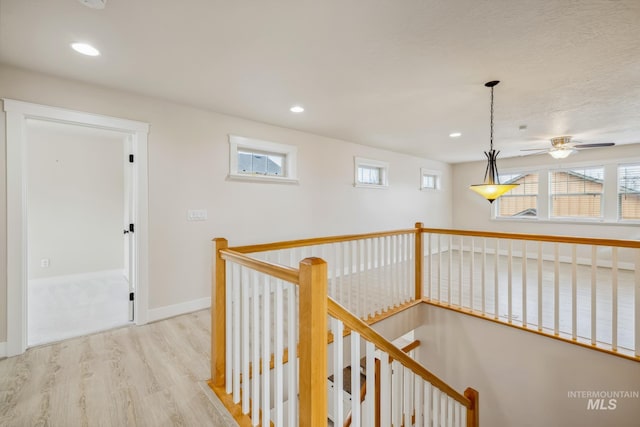 corridor featuring light wood-style floors, recessed lighting, baseboards, and an upstairs landing