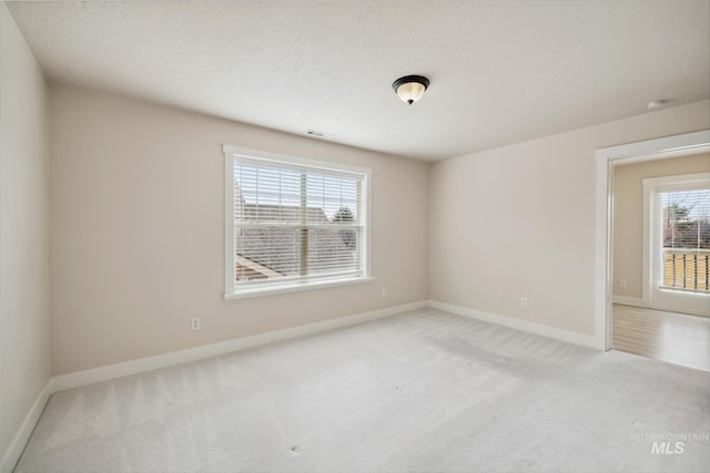 spare room featuring light carpet, visible vents, baseboards, and a textured ceiling