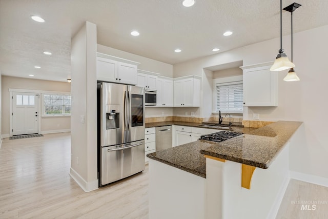 kitchen with pendant lighting, stainless steel appliances, white cabinetry, a sink, and a peninsula