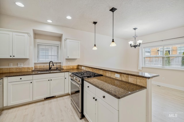 kitchen featuring pendant lighting, stainless steel gas stove, a sink, and white cabinetry