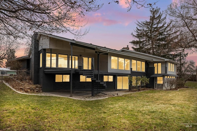 back house at dusk with a patio and a lawn