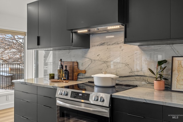 kitchen featuring electric stove, decorative backsplash, light stone counters, and light wood-type flooring