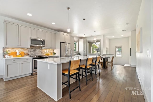 2381 E Warm Spgs, Boise, ID 83712 - kitchen featuring appliances with stainless steel finishes, a center island with sink, backsplash, light countertops, and hardwood / wood-style floors