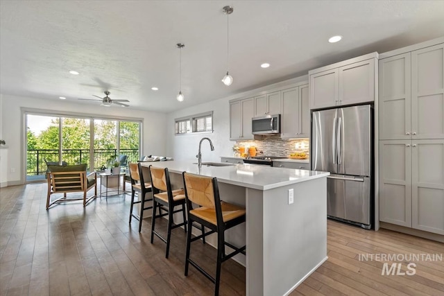2381 E Warm Spgs, Boise, ID 83712 - kitchen with stainless steel appliances, a sink, light wood finished floors, a center island with sink, and tasteful backsplash