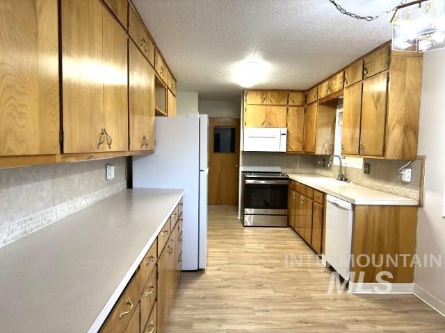 995 E 15th N, Mountain Home, ID 83647 - kitchen featuring a sink, white appliances, light countertops, brown cabinetry, and light wood-type flooring