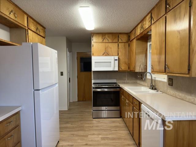 995 E 15th N, Mountain Home, ID 83647 - kitchen featuring white appliances, light wood-type flooring, a textured ceiling, brown cabinets, and a sink