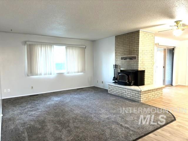 995 E 15th N, Mountain Home, ID 83647 - unfurnished living room with a ceiling fan, a textured ceiling, baseboards, and a wood stove