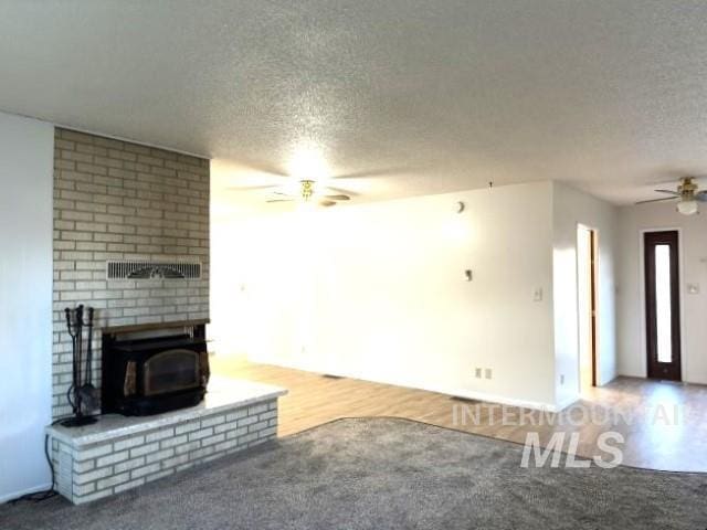 995 E 15th N, Mountain Home, ID 83647 - unfurnished living room with ceiling fan, a textured ceiling, a wood stove, baseboards, and carpet