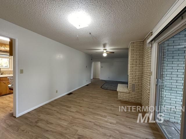995 E 15th N, Mountain Home, ID 83647 - unfurnished room with brick wall, light wood-style floors, baseboards, ceiling fan, and a textured ceiling