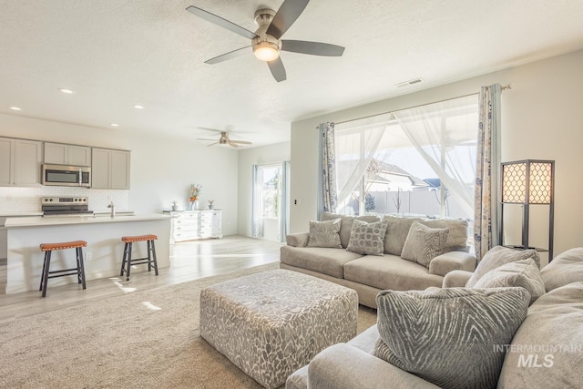 living room with ceiling fan, a textured ceiling, and light wood-type flooring