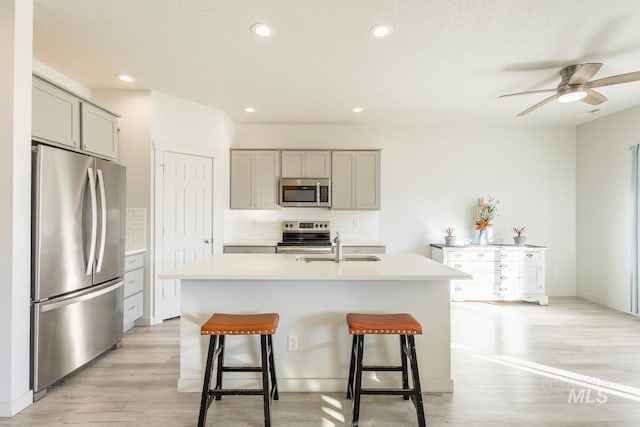 kitchen with gray cabinets, a breakfast bar, appliances with stainless steel finishes, an island with sink, and decorative backsplash