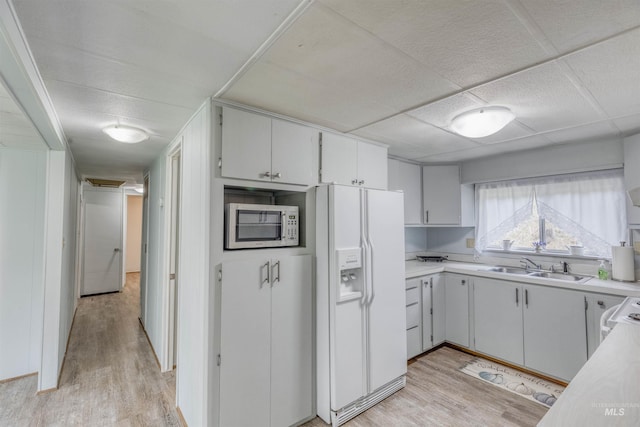 kitchen featuring a sink, light wood finished floors, white fridge with ice dispenser, and light countertops
