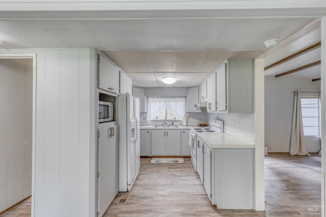 kitchen with light countertops, a sink, under cabinet range hood, white appliances, and light wood-style flooring