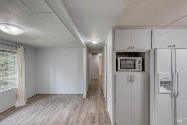 kitchen with light wood finished floors, stainless steel microwave, white refrigerator with ice dispenser, and white cabinets