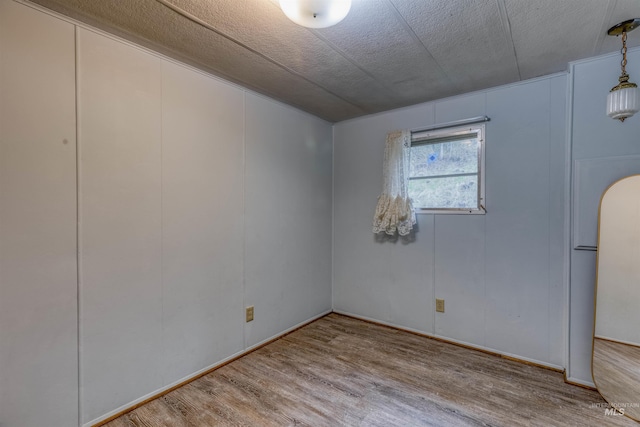 empty room featuring a textured ceiling, a decorative wall, and wood finished floors