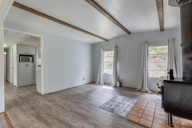 unfurnished living room with vaulted ceiling with beams, a wealth of natural light, and light wood-style floors
