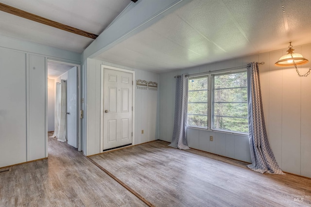 unfurnished bedroom with visible vents, a textured ceiling, a decorative wall, and wood finished floors