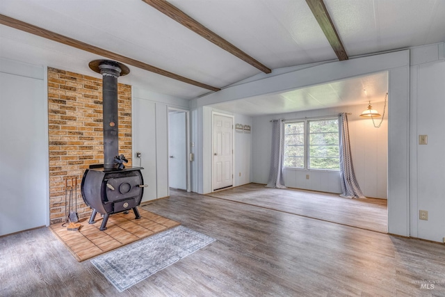 unfurnished living room featuring lofted ceiling with beams, a wood stove, and wood finished floors