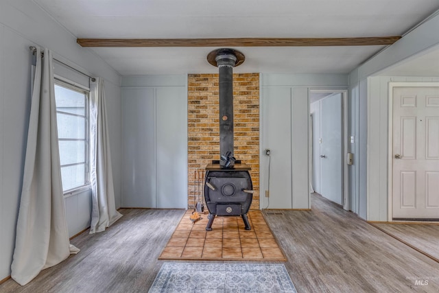 sitting room featuring beamed ceiling, visible vents, wood finished floors, and a wood stove