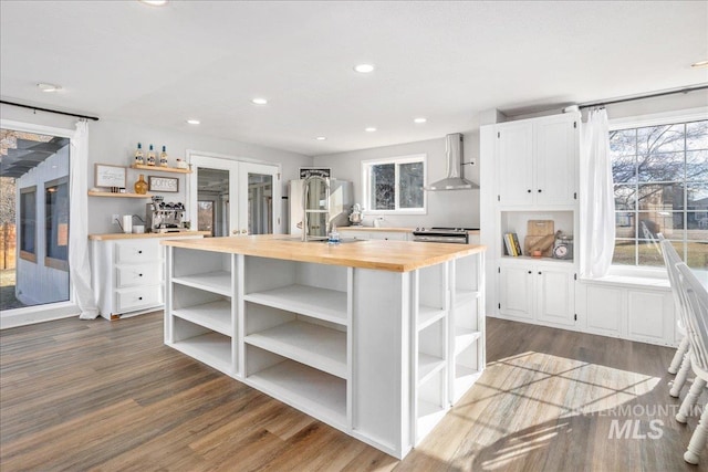 kitchen featuring butcher block counters, dark wood-style floors, white cabinets, wall chimney exhaust hood, and open shelves