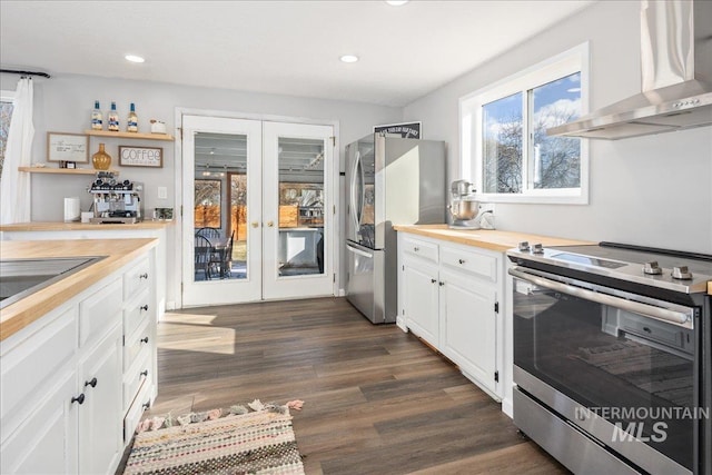 kitchen featuring dark wood-type flooring, wall chimney range hood, appliances with stainless steel finishes, french doors, and white cabinets