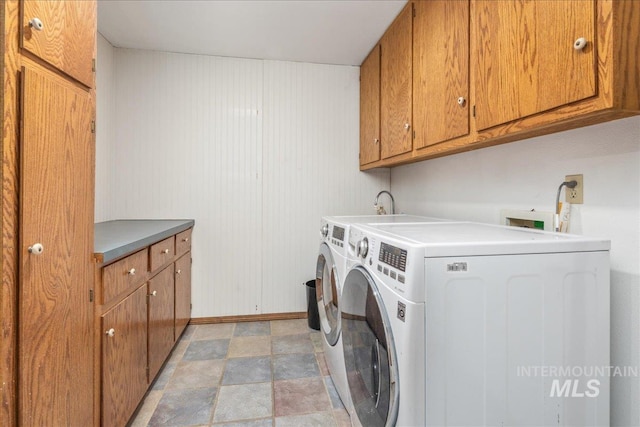 clothes washing area with washing machine and dryer, cabinet space, and baseboards