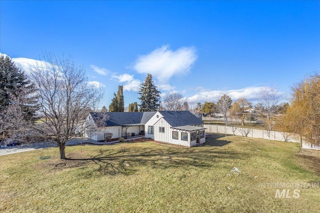 rear view of house with a lawn, board and batten siding, a garage, and fence