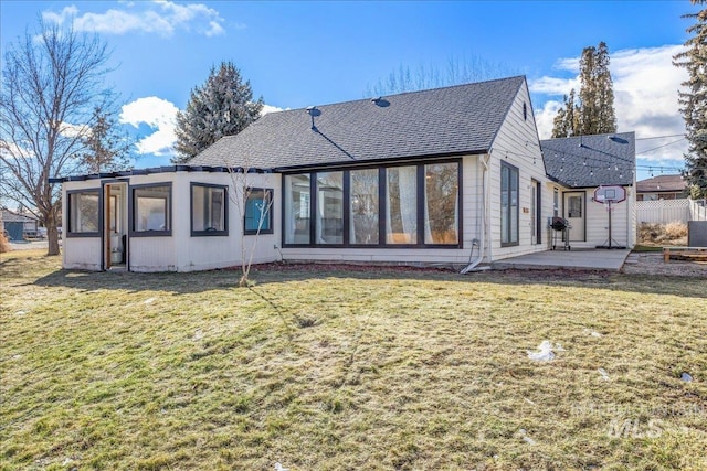 rear view of house featuring a patio area, a lawn, fence, and a shingled roof