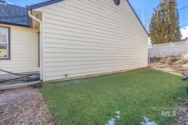 view of side of property featuring fence, a lawn, and a shingled roof