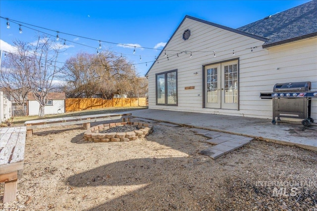 rear view of house with an outdoor fire pit, fence, french doors, a shingled roof, and a patio area