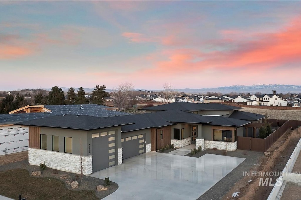 view of front of home featuring fence, a garage, a residential view, stone siding, and driveway