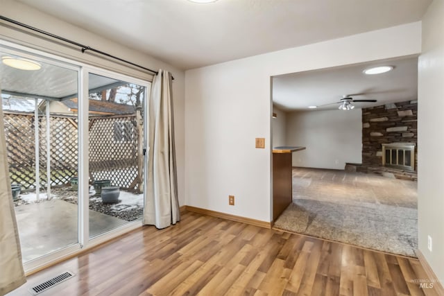 unfurnished room with visible vents, wood finished floors, a stone fireplace, baseboards, and ceiling fan